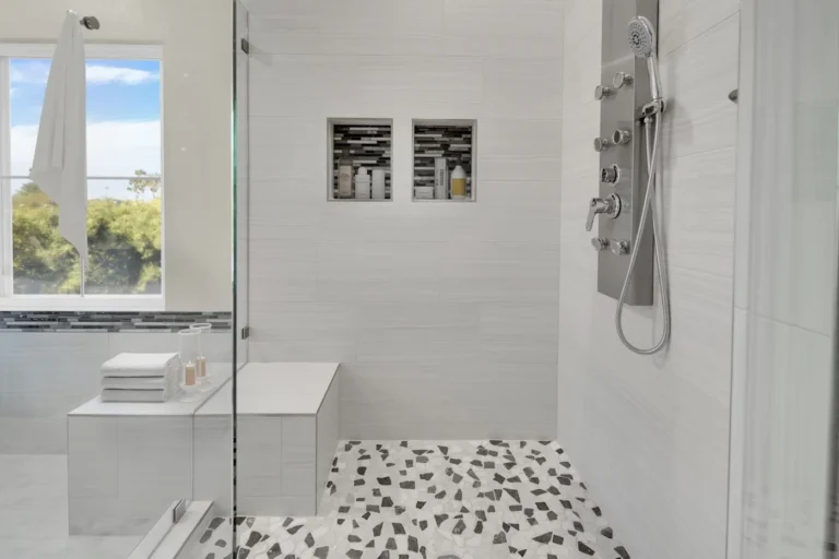 Frameless glass shower with dual tiled niches, a built-in bench and pebble mosaic floor in a Carlsbad bathroom