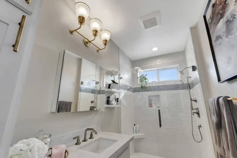 Brushed brass three-light sconce above a mirrored medicine cabinet in a Newport Beach master bathroom