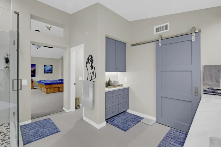 Blue sliding barn door and built-in linen cabinet opening onto the bedroom in a Carlsbad primary bathroom remodel