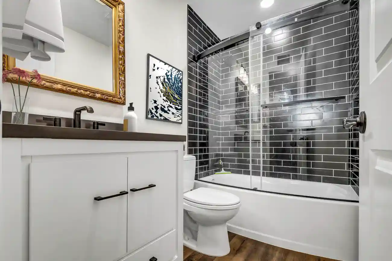 Black subway tile tub shower with curved glass doors in a remodeled Aliso Viejo bathroom with white shaker vanity