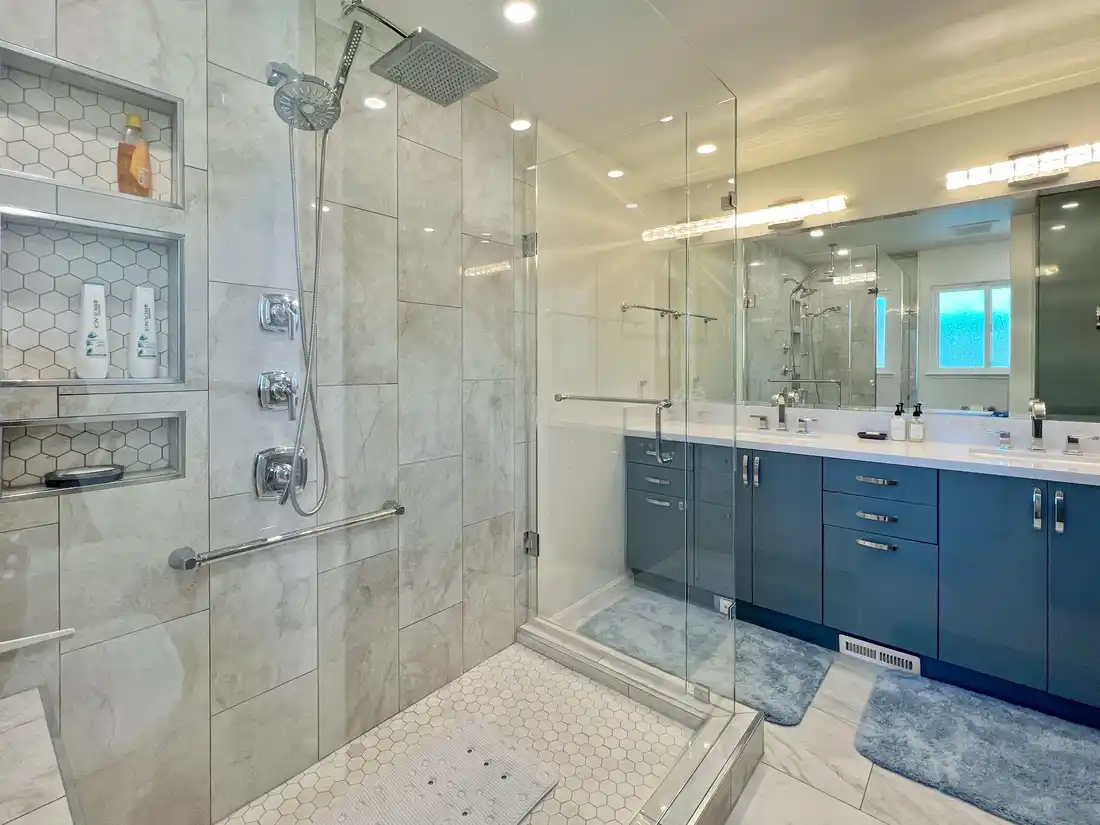 Frameless glass walk-in shower with three hexagon tile niches beside a blue double vanity in an Aliso Viejo bathroom.