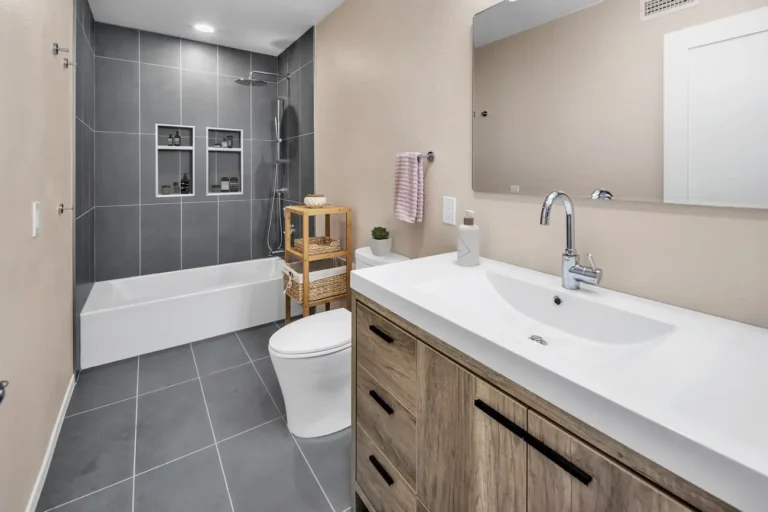 Remodeled Carlsbad bathroom with a gray tiled tub shower combo, wood-look vanity, and white integrated sink
