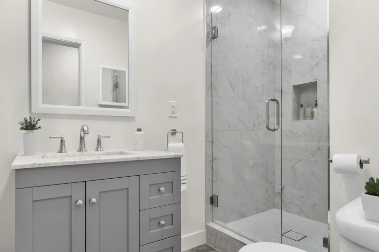 Gray shaker vanity and glass enclosed marble walk-in shower with recessed niche in a finished Irvine bathroom