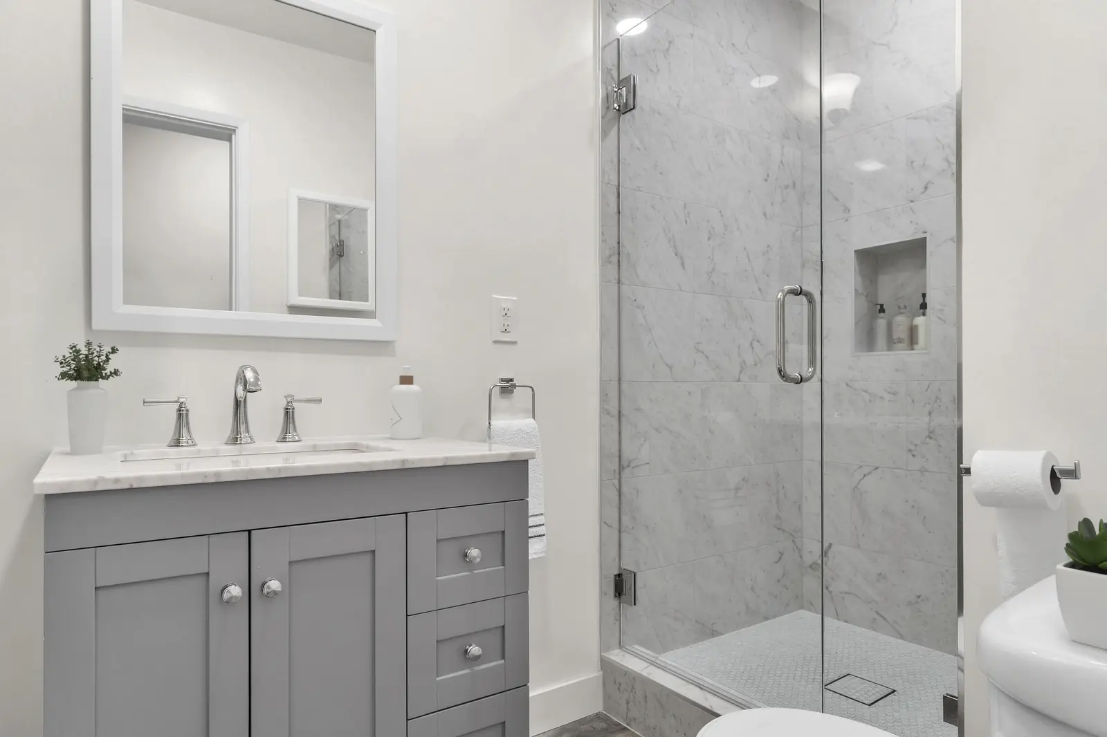 Gray shaker vanity and glass enclosed marble walk-in shower with recessed niche in a finished Irvine bathroom
