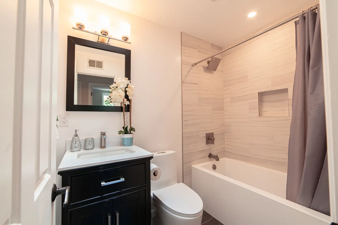Remodeled Irvine bathroom with a black vanity, quartz countertop, tiled tub-shower combo, and dark wood-look floor tile.