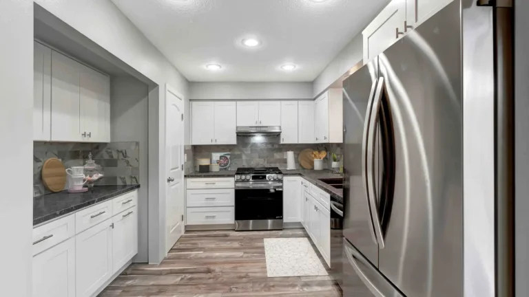 White shaker cabinets, recessed lights, and wood-look plank floors in a wide view of a Huntington Beach kitchen