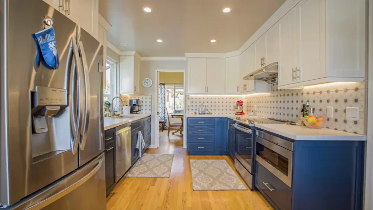 Galley kitchen remodel in Laguna Niguel with white upper cabinets, dark blue lowers, star pattern tile, and wood floors
