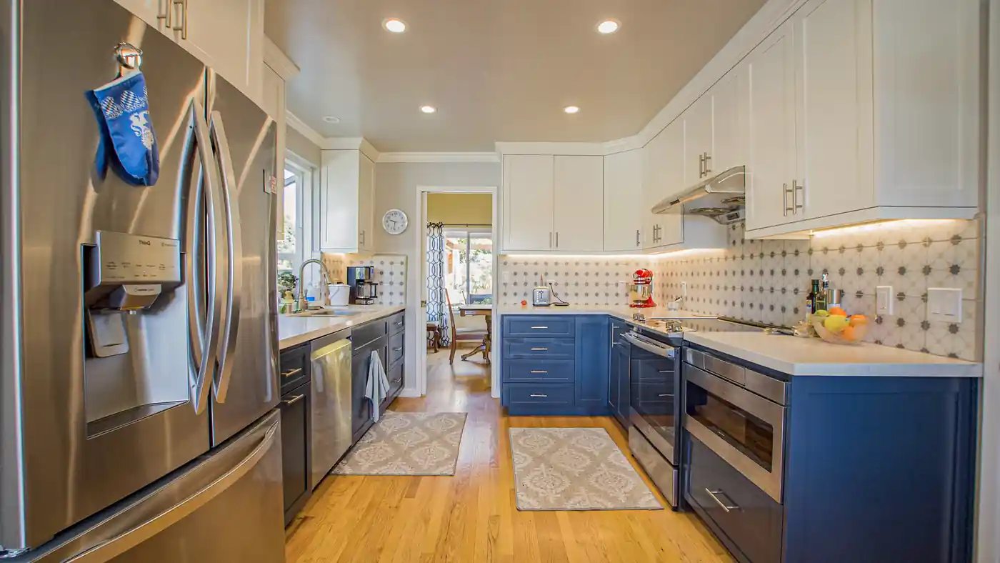 Galley kitchen remodel in Laguna Niguel with white upper cabinets, dark blue lowers, star pattern tile, and wood floors