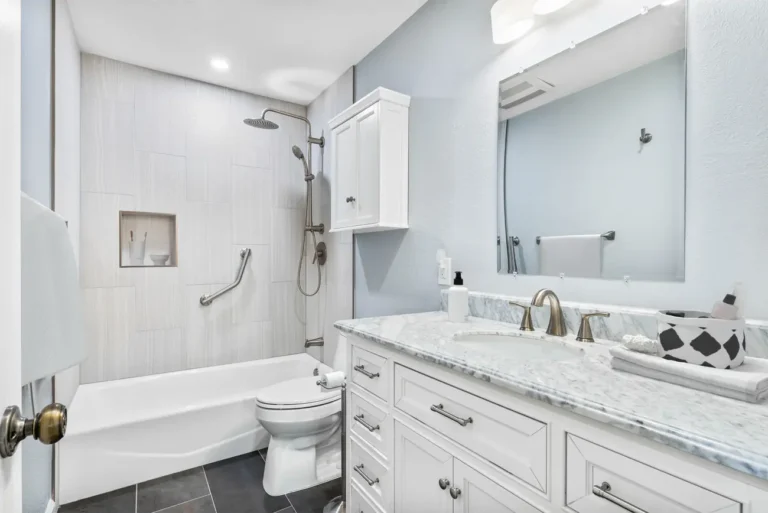 White vanity with a marble top beside a tiled tub shower combo in a remodeled Mission Viejo guest bathroom