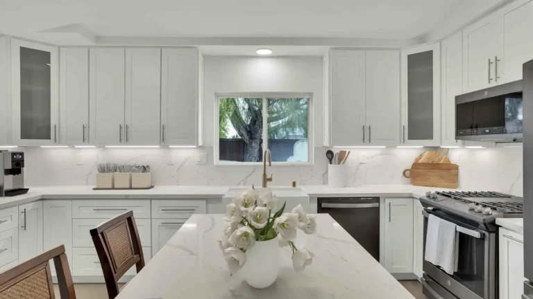Marble-look quartz island facing a white farmhouse sink and brass faucet in a remodeled Oceanside kitchen