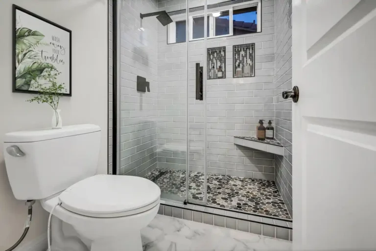 Walk-in shower with gray subway tile and pebble stone floor beside the toilet in a San Clemente bathroom remodel