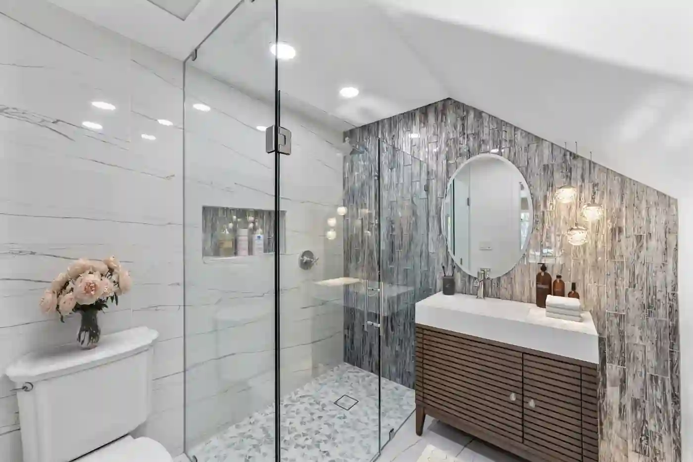 Frameless glass shower with marble-look tile beside a slatted wood vanity in a Santa Ana guest bathroom remodel