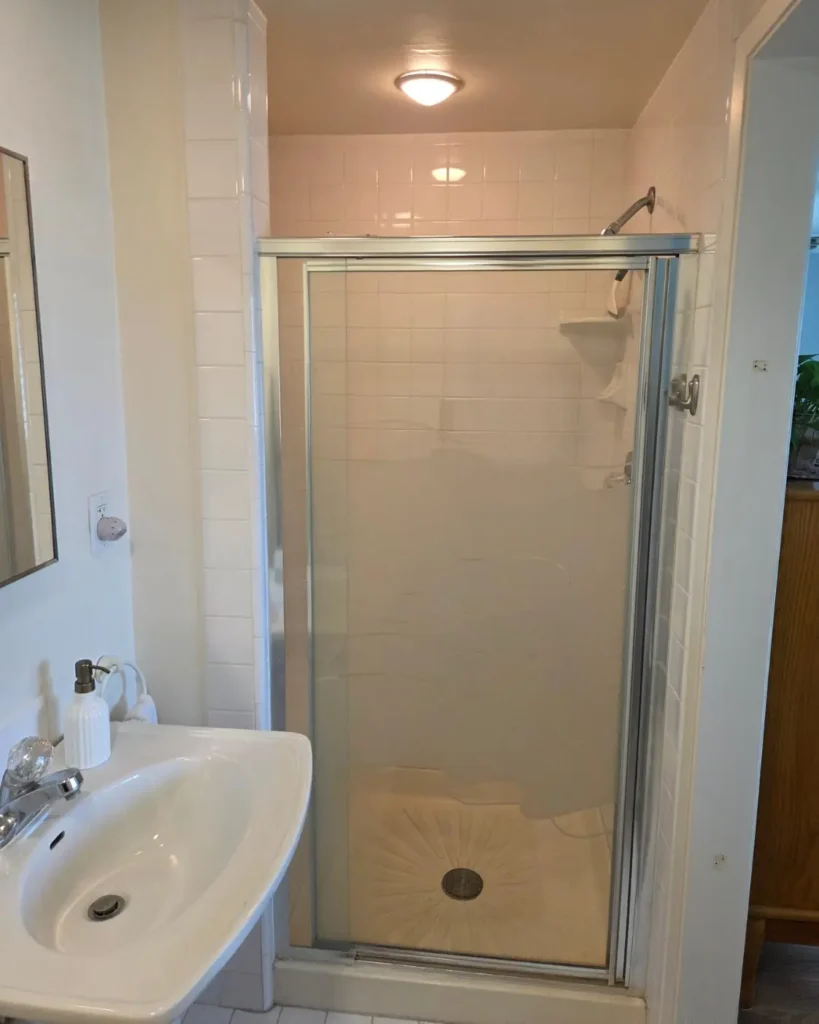 Before photo of a Cypress master bathroom showing the original framed walk-in shower with white tile and an older glass enclosure.