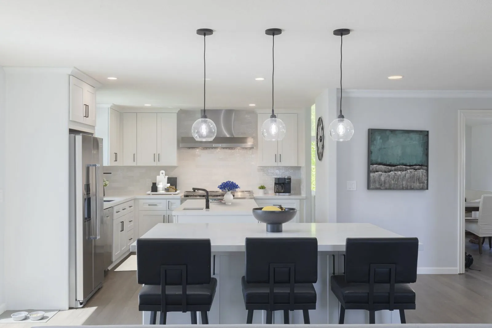 Two white quartz islands with black leather counter stools and glass globe pendants in a Newport Beach kitchen remodel