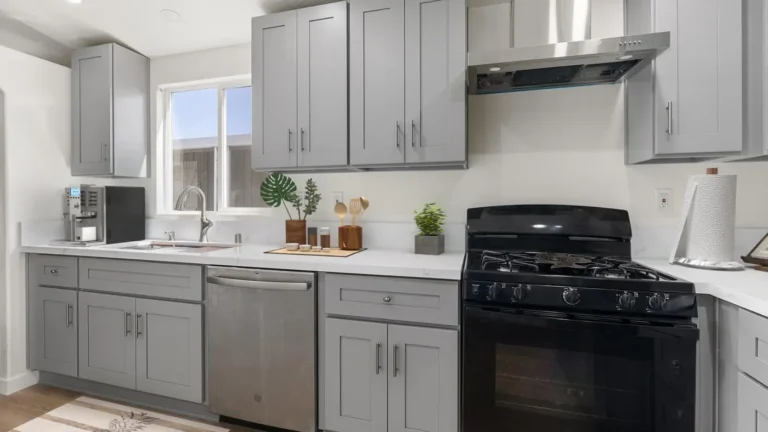 Black gas range under a stainless chimney hood between gray shaker cabinets in a remodeled Torrance kitchen