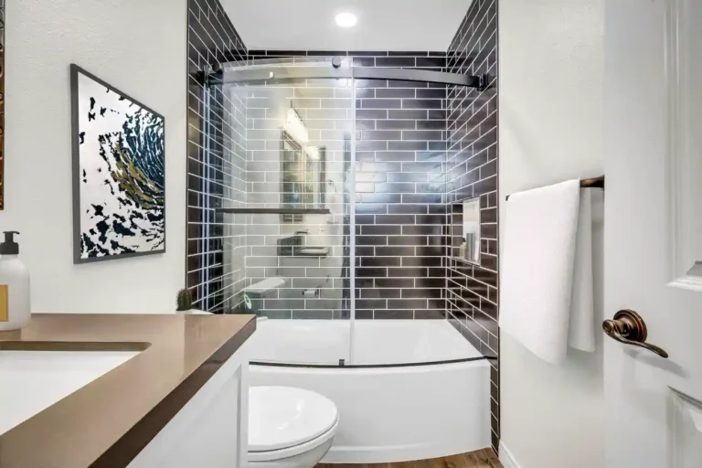 Curved glass tub enclosure framed by black subway tile in an Aliso Viejo bathroom remodel with fresh white towels
