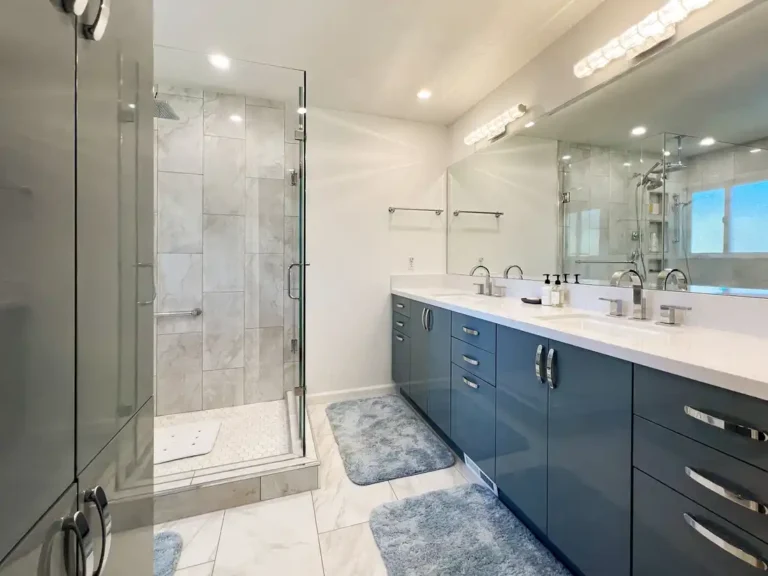 Blue gloss double vanity with white quartz countertop facing a frameless glass shower in an Aliso Viejo bathroom.