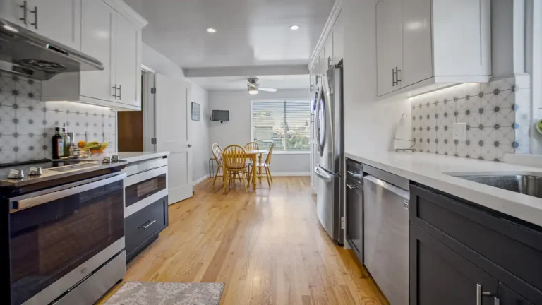 Galley walkway with wood floors leading to a dining nook in a Laguna Niguel kitchen, flanked by stainless appliances