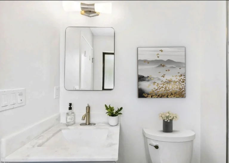 Gray vanity with a marble countertop, brushed gold faucet, and rounded frameless mirror in a Laguna Niguel bathroom