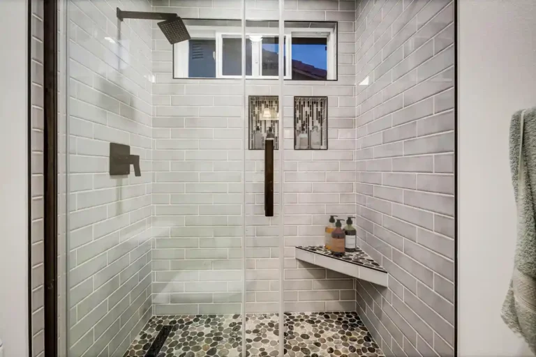 Rainfall showerhead and clear glass doors above a pebble tile shower floor in a San Clemente bathroom remodel