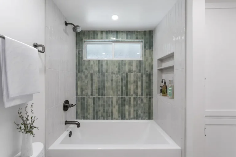 Vertical green tile accent wall and shower niche above a white soaking tub in a Santa Ana guest bathroom remodel.