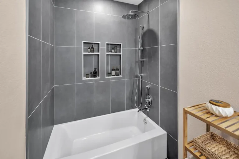 Tub and shower combo with gray tile walls, twin recessed niches, and a rainfall showerhead in a Carlsbad bathroom