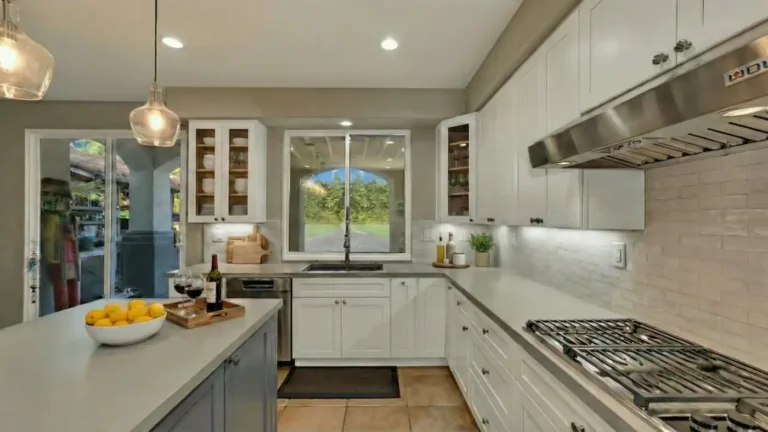 Gray quartz island facing a window sink wall, glass-front cabinets, and a gas cooktop in a remodeled Carlsbad kitchen.