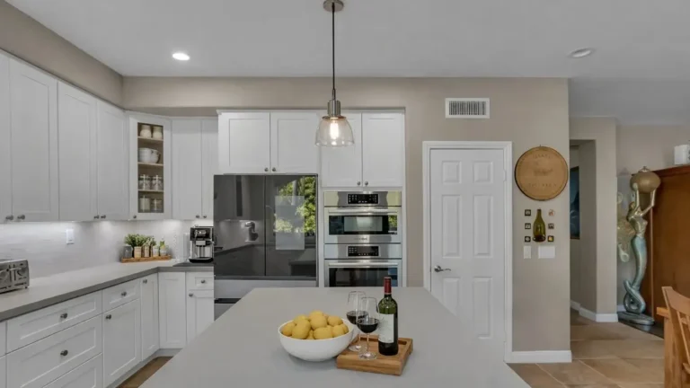 Large gray quartz island facing a French-door refrigerator and stainless double wall ovens in a Carlsbad kitchen.