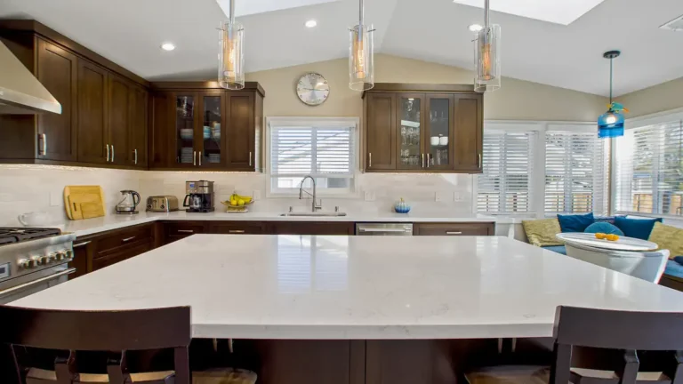 White quartz island countertop under glass pendant lights and glass-front shaker cabinets in an Irvine kitchen remodel