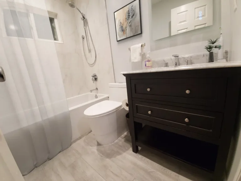 Dark vanity with a marble countertop and LED mirror beside the tiled tub shower in a Lake Forest bathroom.