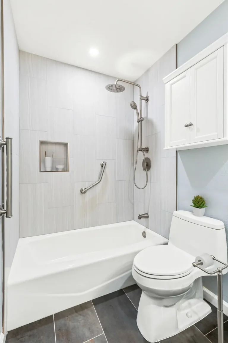 Tub shower combo with vertical tile and a one-piece toilet under a white wall cabinet in a Mission Viejo guest bath