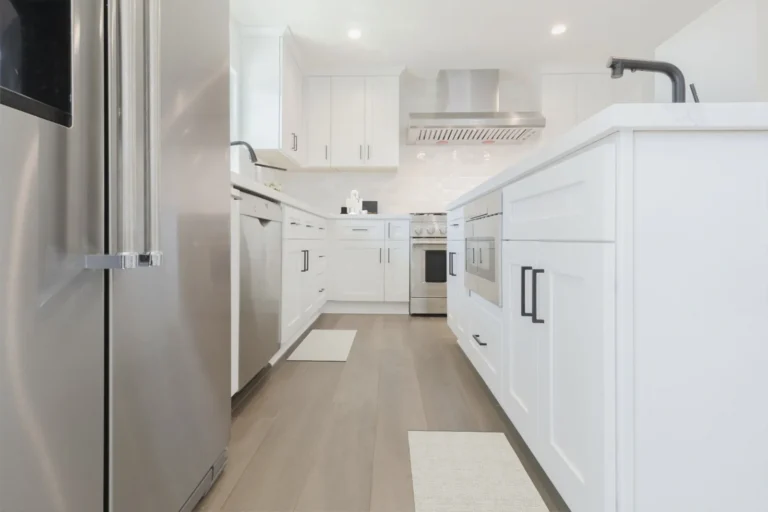 Stainless refrigerator beside a white shaker island with a built-in microwave in a Newport Beach kitchen remodel