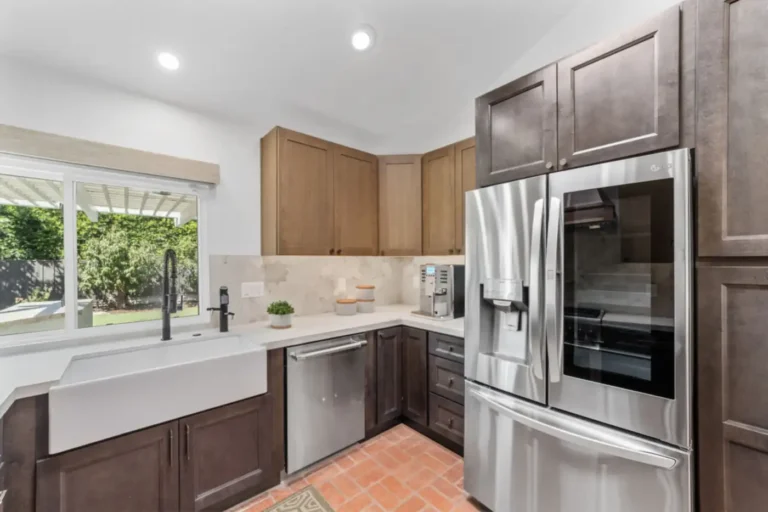 White farmhouse sink with a black pull-down faucet beneath a window beside a French door refrigerator in Santa Ana