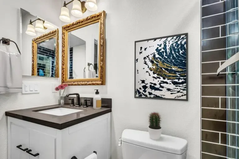 Gold framed mirror and three light fixture above a white vanity in a remodeled Aliso Viejo guest bathroom