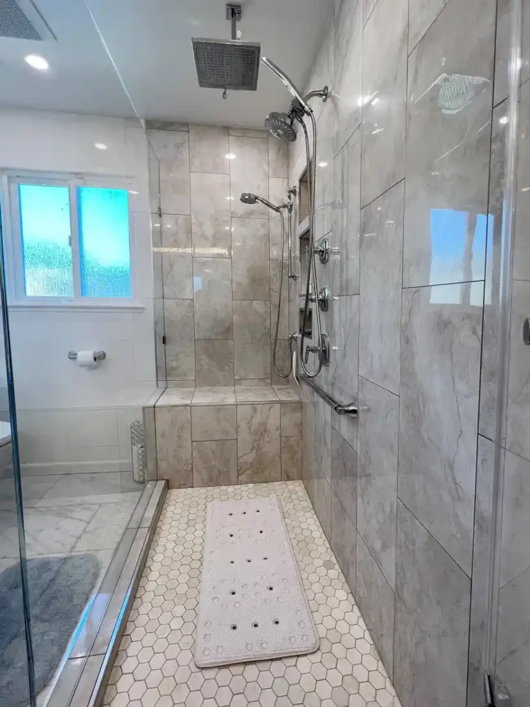 Ceiling mounted rain shower head above a tiled built-in bench in an Aliso Viejo bathroom walk-in shower.