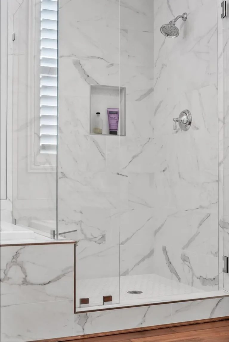 Recessed shampoo niche and polished chrome shower head inside the frameless glass shower of a Carlsbad bathroom.