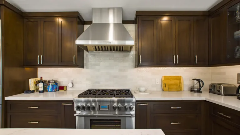 Stainless chimney hood over a professional gas range and glazed subway tile backsplash in a custom Irvine kitchen