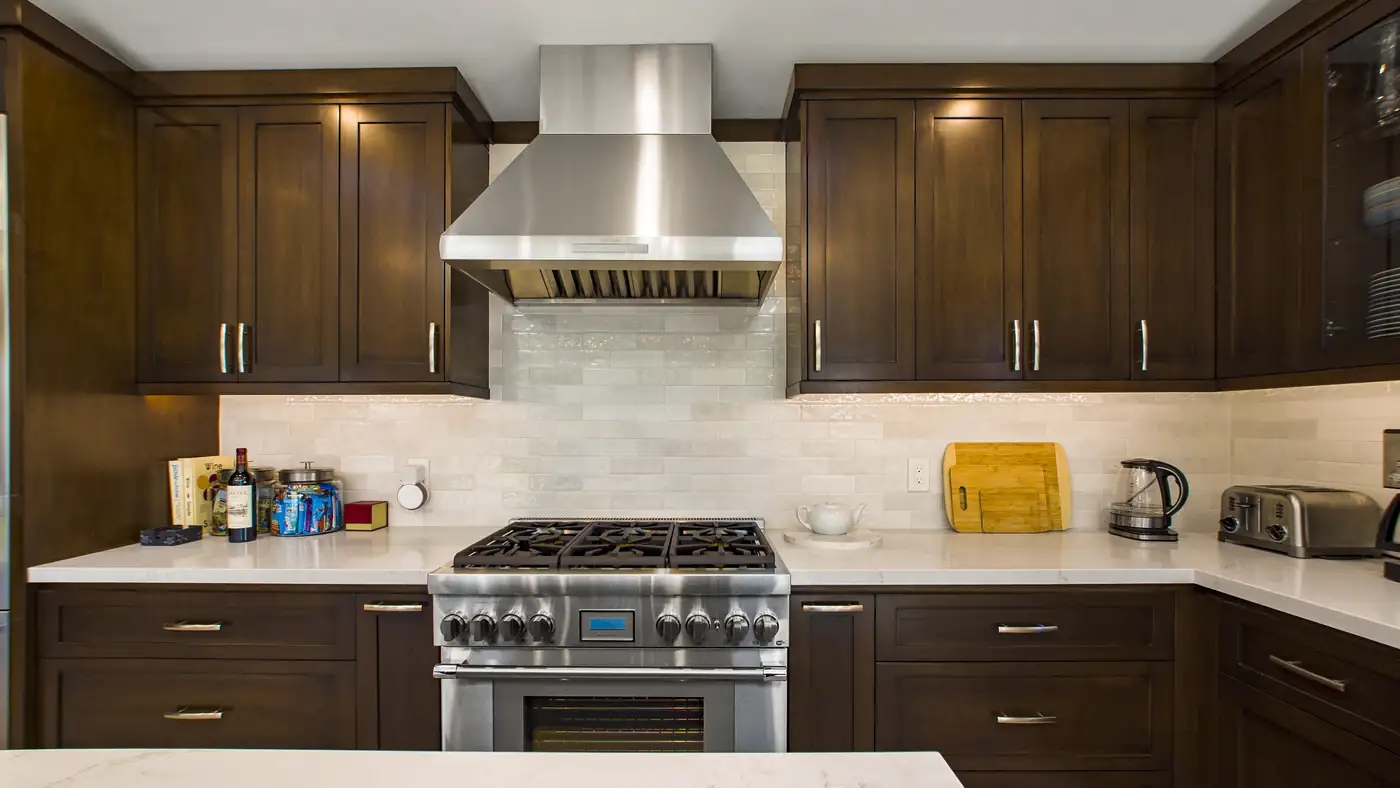 Stainless chimney hood over a professional gas range and glazed subway tile backsplash in a custom Irvine kitchen