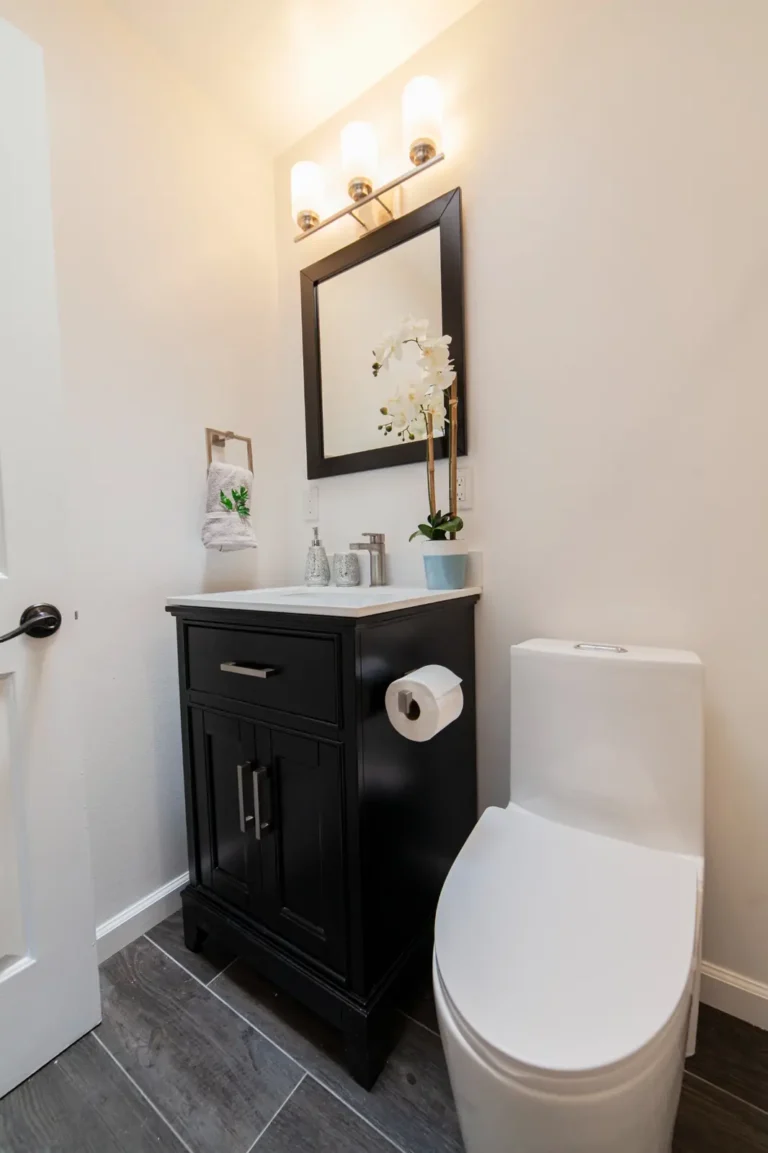Black vanity with white quartz countertop and framed mirror beside the toilet in an Irvine bathroom remodel.