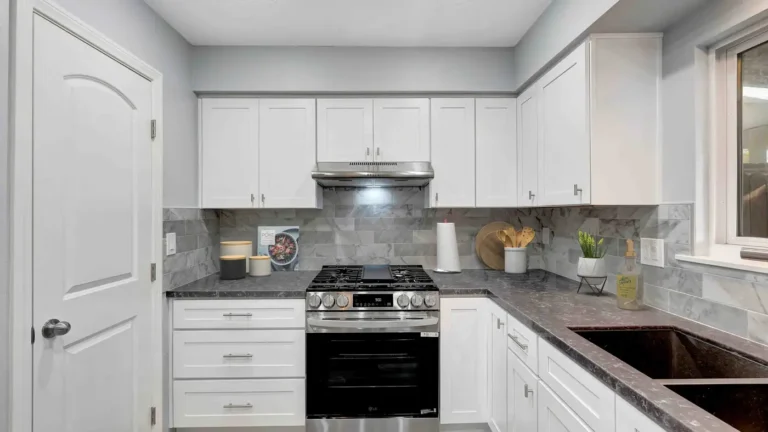 Stainless gas range and vent hood with white shaker cabinets and gray marble-look tile in a Huntington Beach kitchen