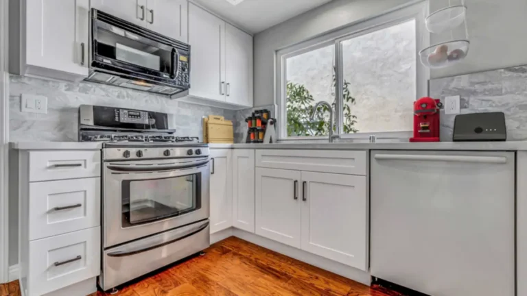 Stainless gas range under a black microwave, framed by white shaker cabinets and gray tile in an Irvine kitchen remodel.