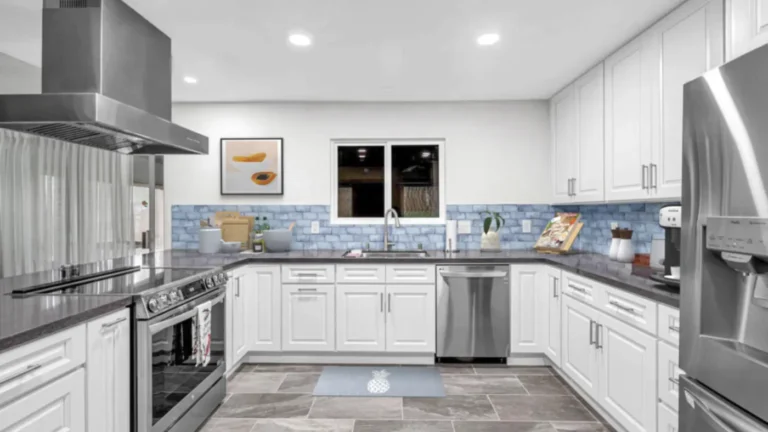 Blue patterned tile backsplash wrapping a U-shaped run of white raised panel cabinets in a Laguna Hills kitchen remodel