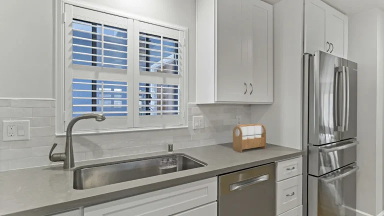 Undermount stainless sink under a shuttered window with gray countertops in a remodeled Laguna Hills kitchen