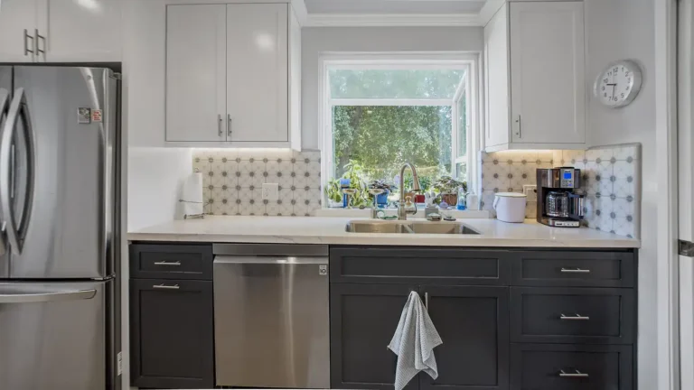 Double basin sink under a garden window with star pattern tile and dark blue shaker cabinets in a Laguna Niguel kitchen