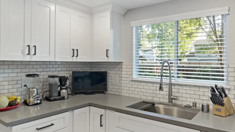 Stainless workstation sink below a wide window with white subway tile in the corner of a Laguna Niguel kitchen remodel