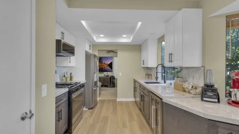 Tray ceiling with recessed lighting over a two-tone galley kitchen in Oceanside with stainless steel appliances