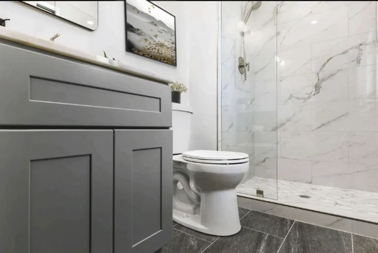 Gray shaker vanity and dark gray floor tile beside a curbed marble shower in a Laguna Niguel bathroom remodel