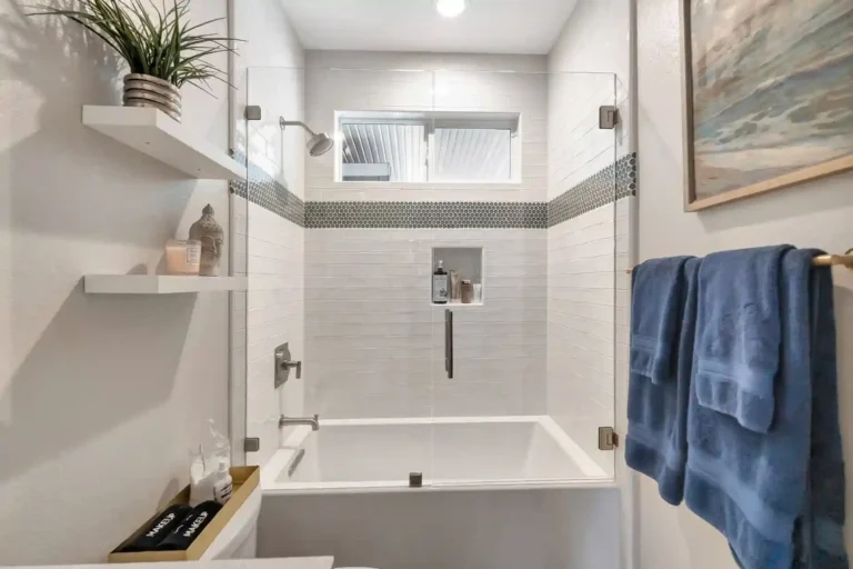 Glass enclosed tub with recessed shower niche and gray penny tile border in a Newport Beach guest bathroom