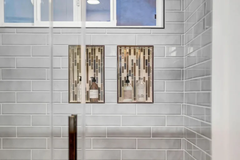 Twin recessed shower niches lined with vertical glass mosaic tile below a window in a San Clemente bathroom remodel