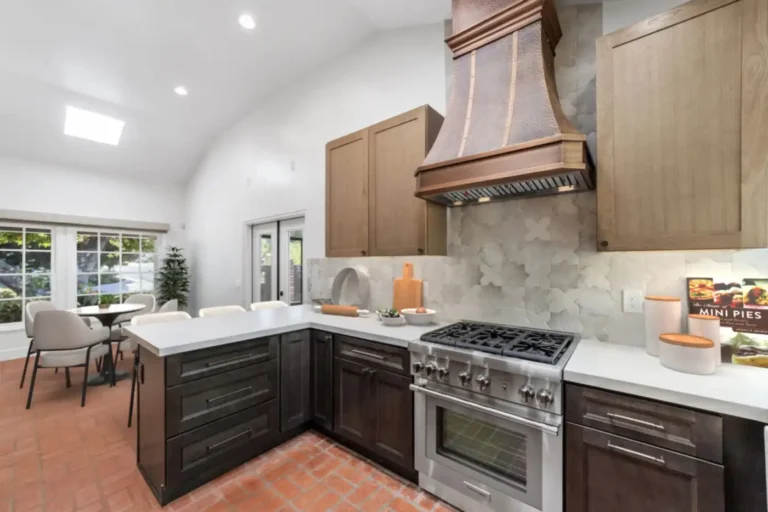 Quartz peninsula with dark drawer cabinets next to a pro-style gas range under a copper hood in a Santa Ana kitchen